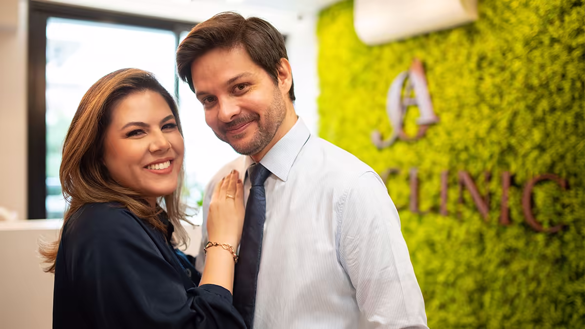 Dra. Aline Soares e Dr. Osório Lara lado a lado diante da parede de vegetação da recepção.