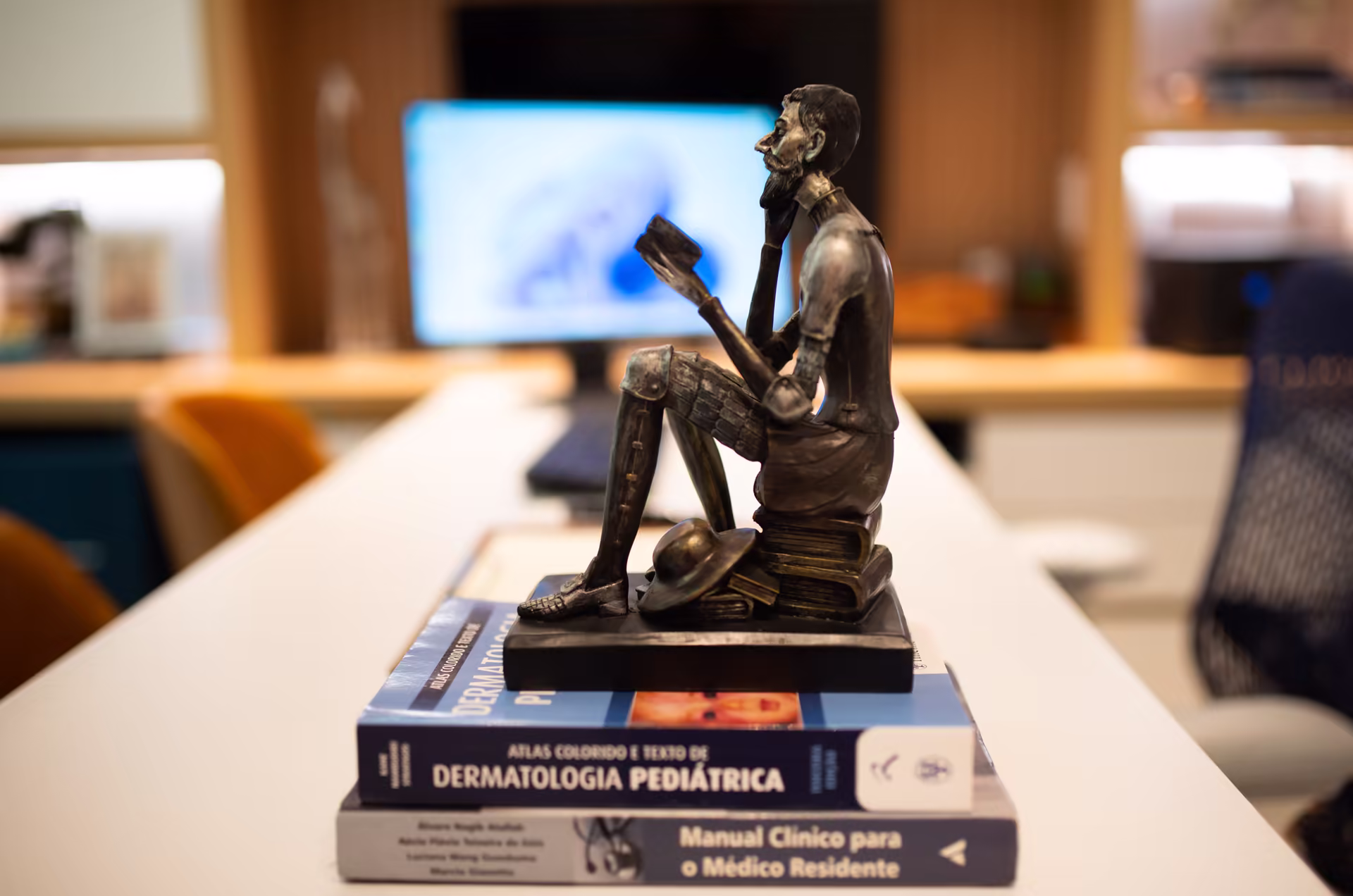 Escultura de bronze sobre uma pilha de livros de dermatologia, na bancada do consultório.